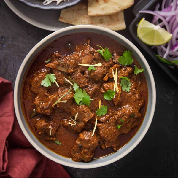 Overhead view of a bowl of rich, dark brown curry with meat, garnished with cilantro and ginger.