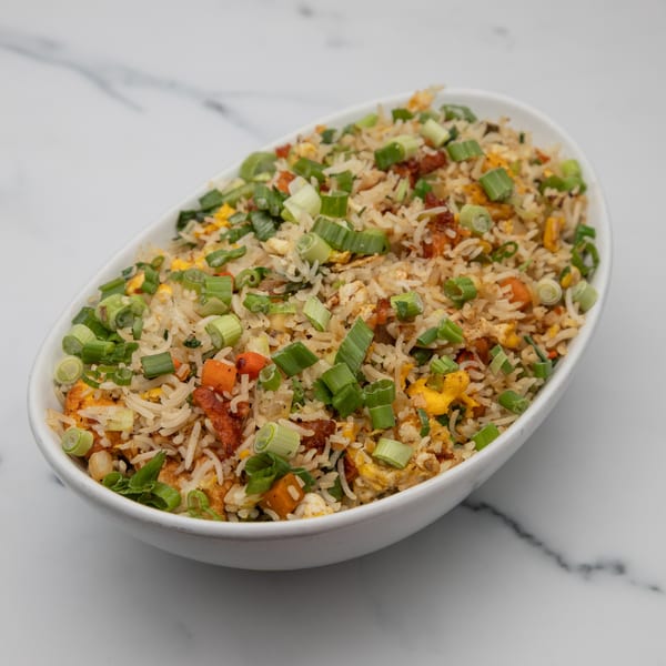 A white oval bowl filled with Indian fried rice, garnished with chopped green onions.