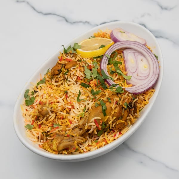 Mintt Indian Cuisine's chicken biryani, garnished with red onion, lemon, and cilantro, in a white bowl.