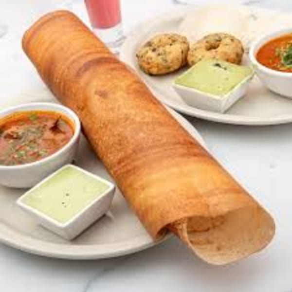 A golden-brown dosa roll with two bowls of chutney, two bowls of sambar, and two vada on a plate.