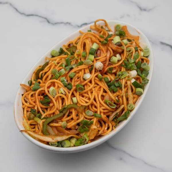 A white oval bowl filled with Indian noodles, green onions, and vegetables on a marble surface.