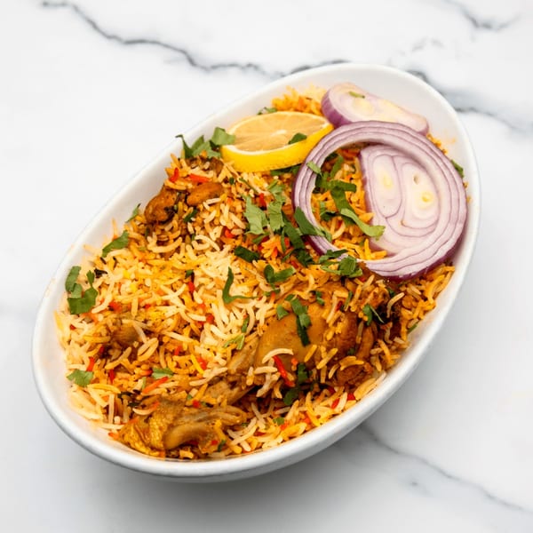 Mintt Indian Cuisine's chicken biryani, garnished with red onion, lemon, and cilantro, in a white bowl.