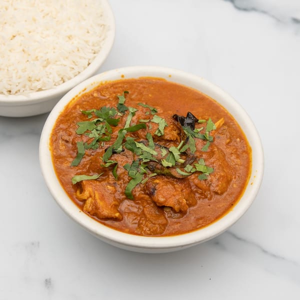 A bowl of Mintt Indian Cuisine's chicken curry with cilantro, next to a bowl of white rice.