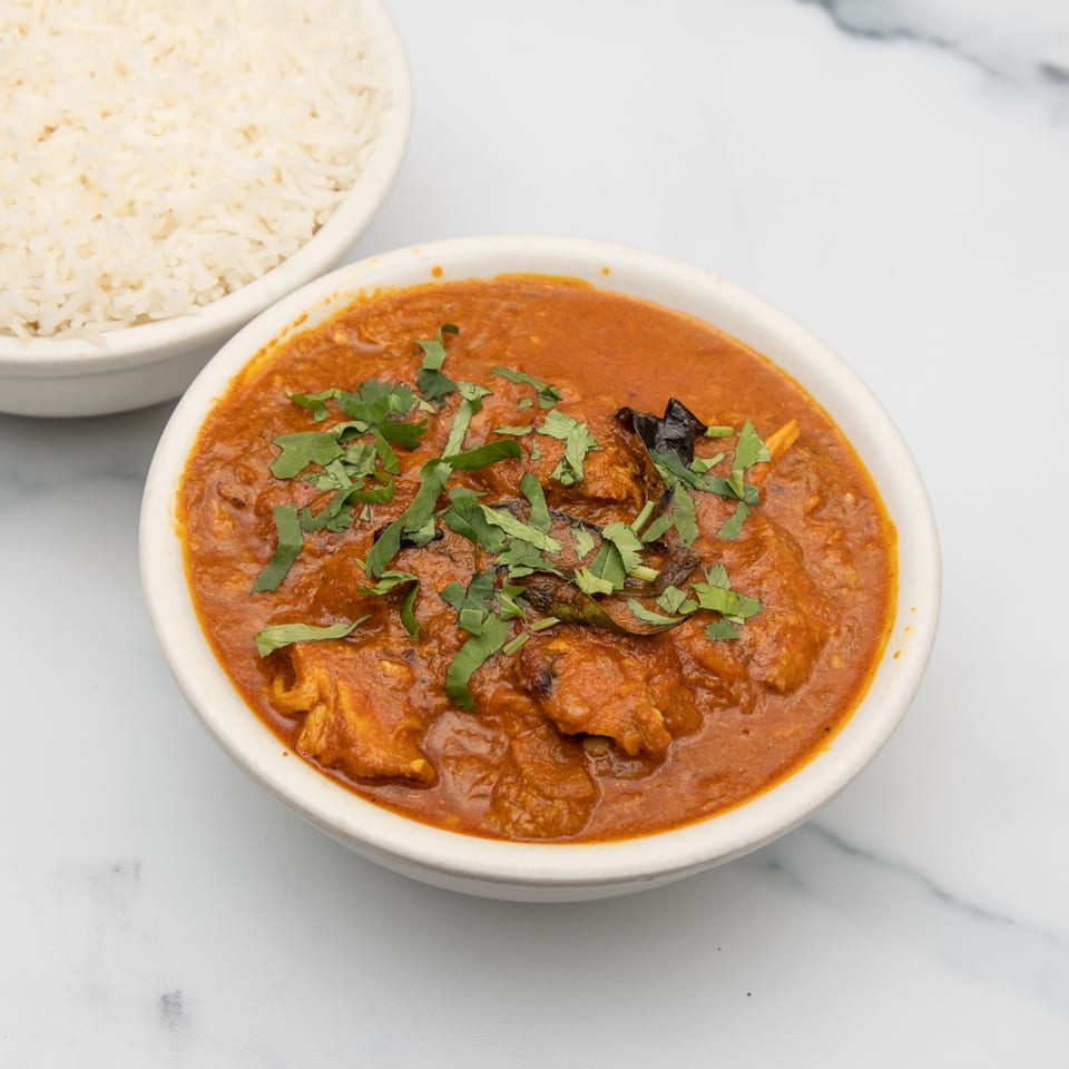 A bowl of Mintt Indian Cuisine's chicken curry with cilantro, next to a bowl of white rice.