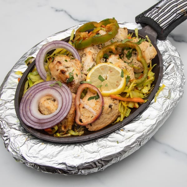 Indian chicken tikka sizzler with onions, bell peppers, and lemon on a foil-wrapped platter.