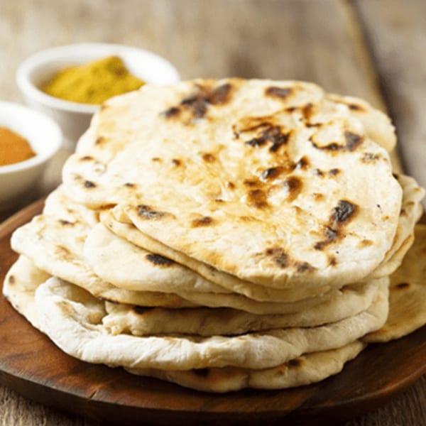 Stack of freshly baked naan bread on a wooden board, with small bowls of spices in the background.