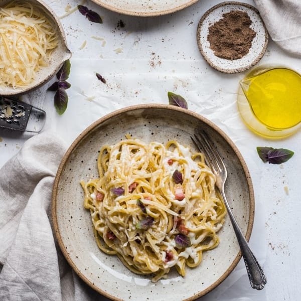 Creamy pasta with bacon and purple basil, surrounded by grated cheese, pepper, and olive oil.