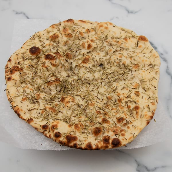 Round, golden-brown rosemary naan bread from Mintt Indian Cuisine, on white parchment paper.