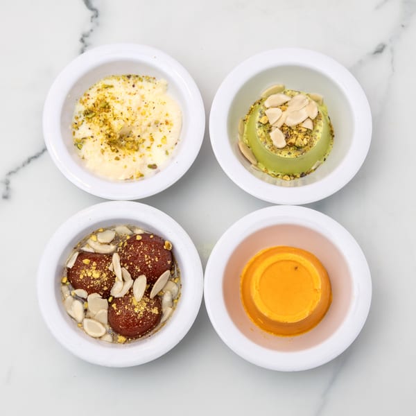 Four bowls of Indian desserts: kheer, pistachio kulfi, gulab jamun, and mango kulfi.