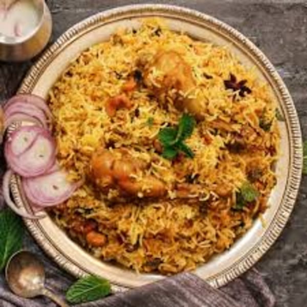 Chicken biryani with mint, star anise, and red onion on a silver platter.