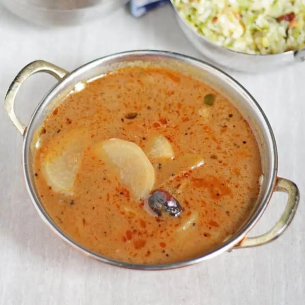 A metal bowl filled with a rich orange curry, containing potato chunks and spices.