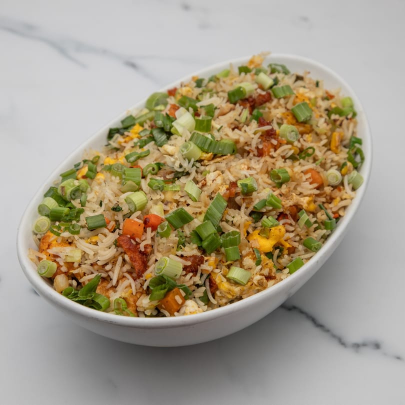 A white oval bowl filled with Indian fried rice, garnished with chopped green onions.