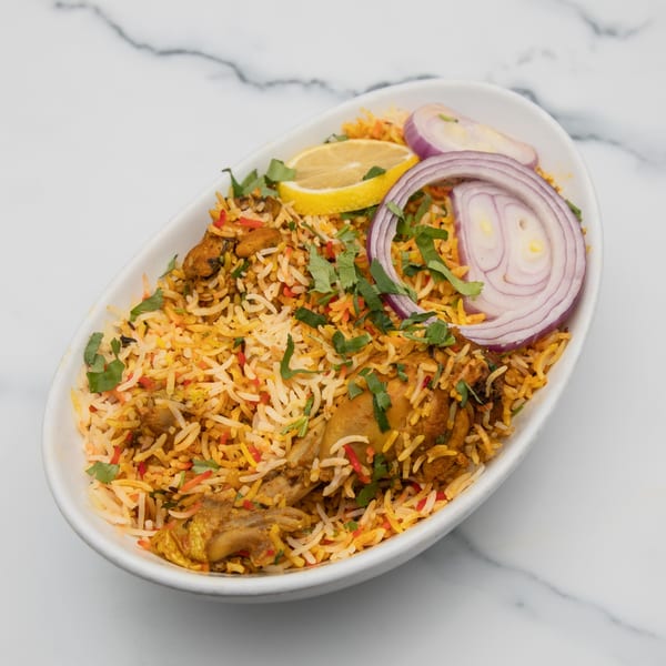 Mintt Indian Cuisine's chicken biryani with rice, chicken, lemon, red onion, and cilantro.