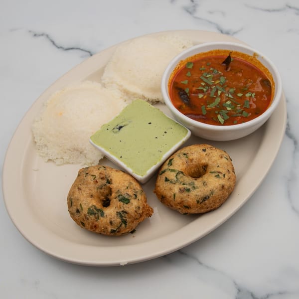 A plate of Mintt Indian Cuisine's idli, vada, sambar, and green chutney on a marble surface.