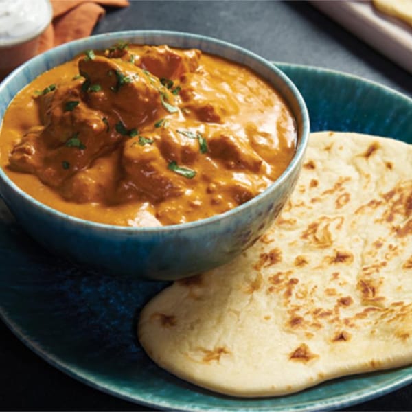 Chicken tikka masala in a blue bowl with naan bread on a matching plate.
