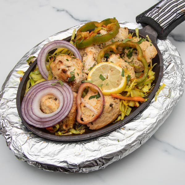 Mintt Indian Cuisine's chicken tikka sizzler with onions, bell peppers, and lemon on a hot plate.