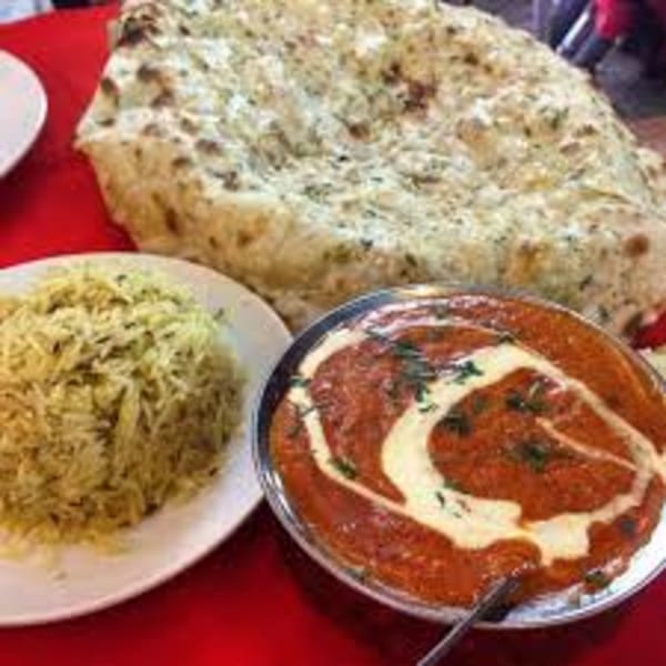 Indian meal with butter chicken, basmati rice, and naan bread on a red tablecloth.