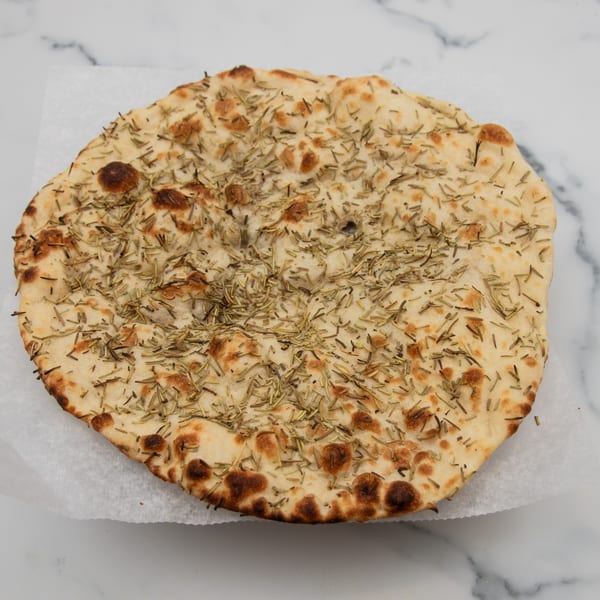 Round rosemary naan bread with golden brown spots, resting on white parchment paper.