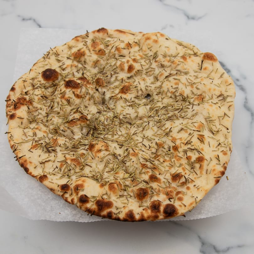 Round rosemary naan bread with golden brown spots, resting on white parchment paper.