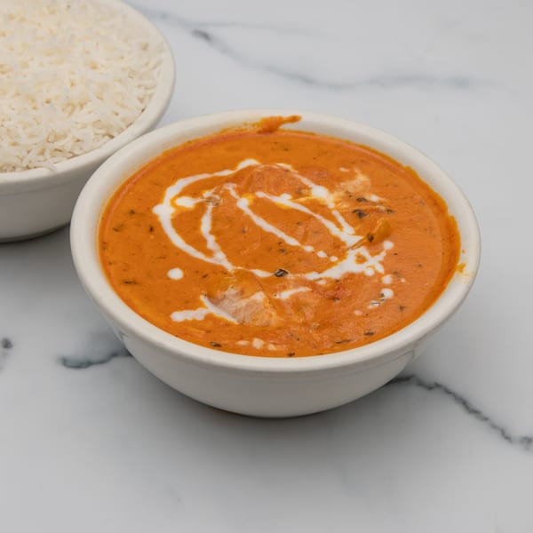 A bowl of creamy orange Indian curry with white swirls, next to a bowl of white rice.