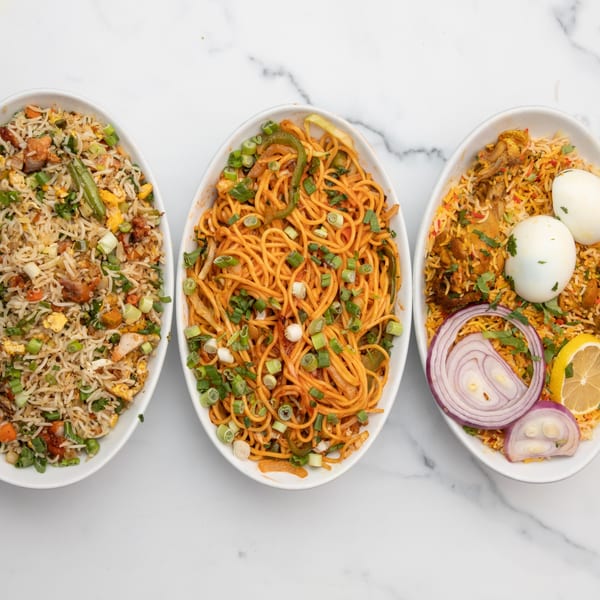 Three Indian dishes: fried rice, noodles, and biryani with eggs, onions, and lemon.