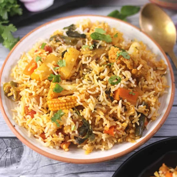 A close-up of vegetable biryani with rice, cauliflower, baby corn, and other vegetables.
