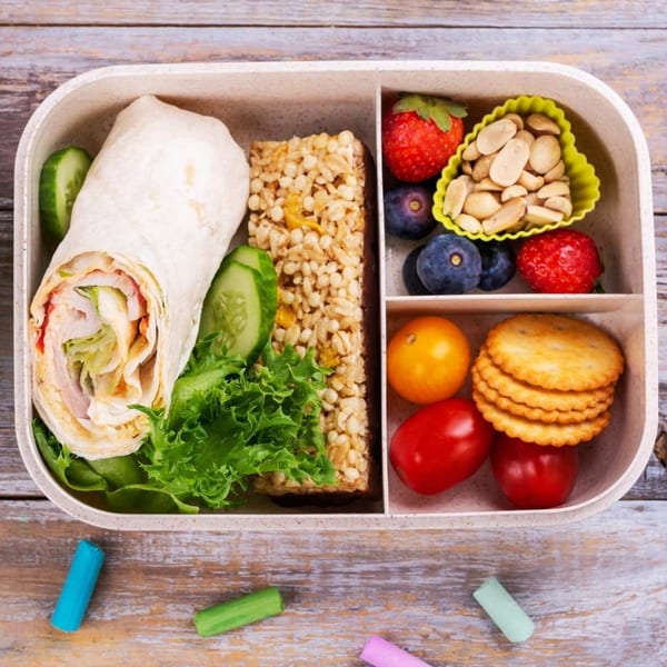 A bento box filled with a wrap, granola bar, berries, peanuts, crackers, and cherry tomatoes.