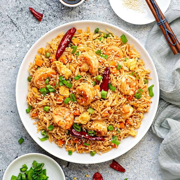 Shrimp fried rice with vegetables, sesame seeds, and red chili peppers on a white plate.