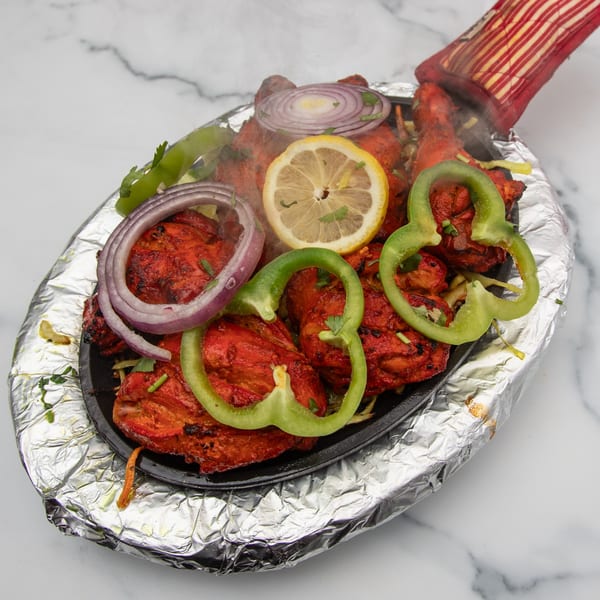 Sizzling Mintt Indian Cuisine tandoori chicken, garnished with onions, bell peppers, and lemon slices.