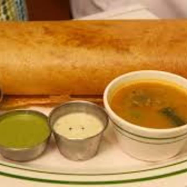 A golden-brown dosa served with three small bowls of green chutney, white chutney, and sambar.