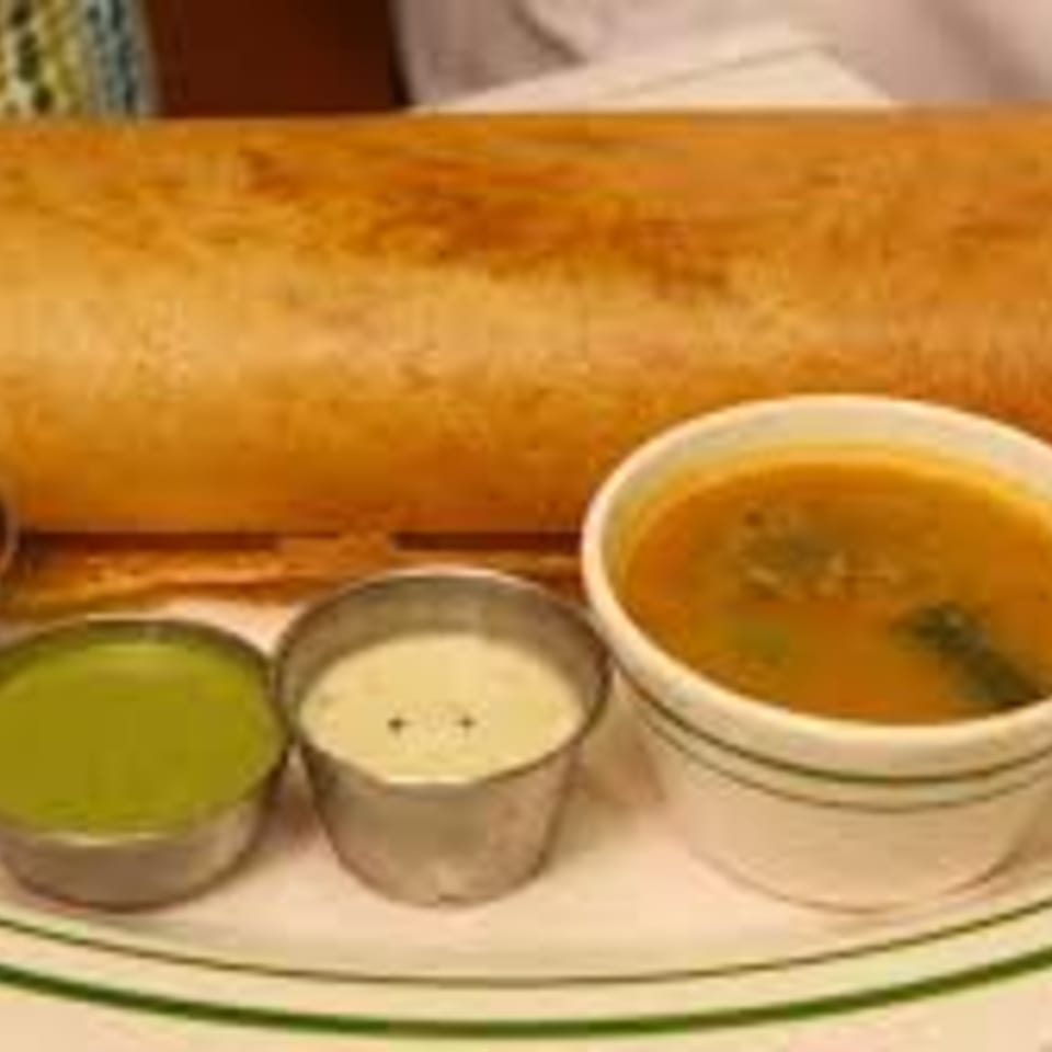 A golden-brown dosa served with three small bowls of green chutney, white chutney, and sambar.