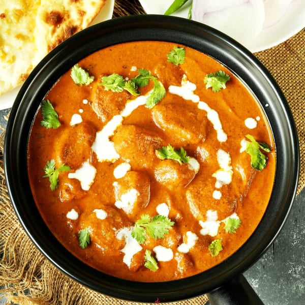 Overhead view of butter chicken in a black bowl, garnished with cream and cilantro, with naan bread.