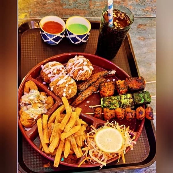A platter of diverse appetizers, including fries, skewers, fried balls, and sauces, with a drink.