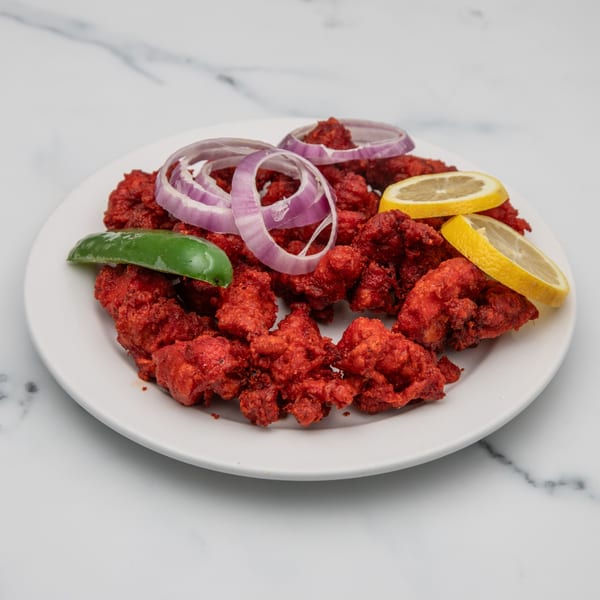 Mintt Indian Cuisine's bright red Chicken 65, garnished with onion rings, lemon slices, and a green chili.