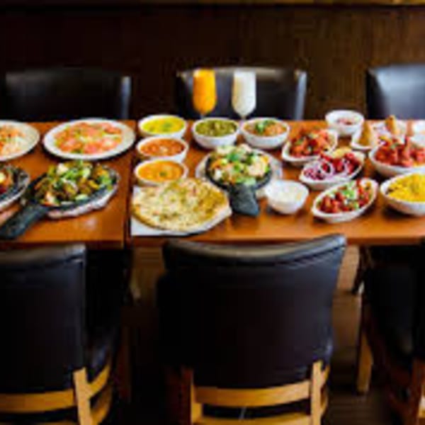 A long table laden with various Indian dishes, including curries, naan bread, and drinks.