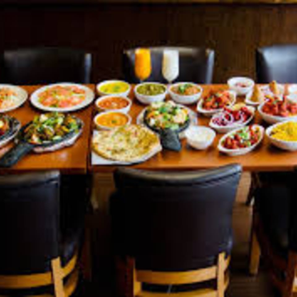 A long table laden with various Indian dishes, including curries, naan bread, and drinks.