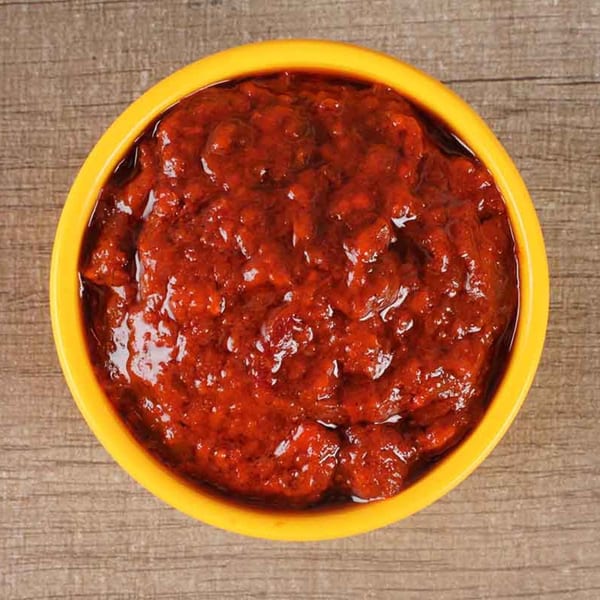 Bright red chili garlic sauce in a yellow bowl on a wooden surface.