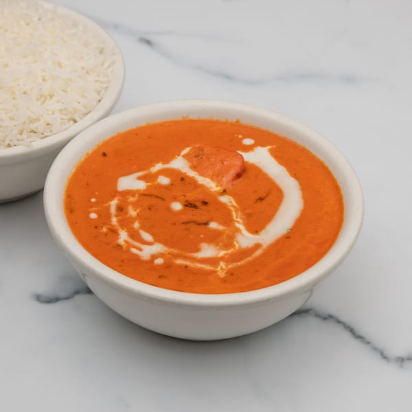 A bowl of Mintt Indian Cuisine's orange butter chicken with cream swirls, next to white rice.