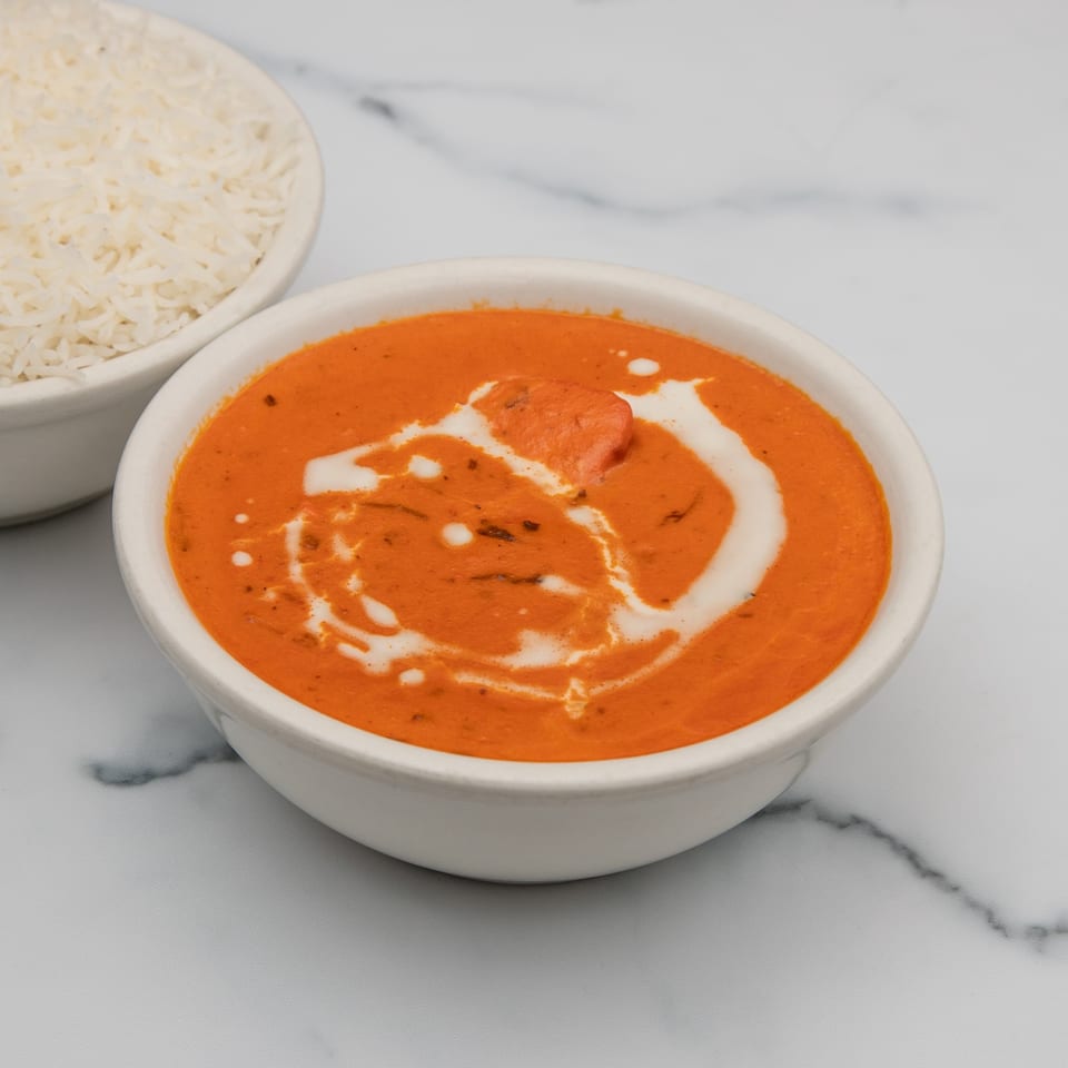 A bowl of Mintt Indian Cuisine's orange butter chicken with cream swirls, next to white rice.