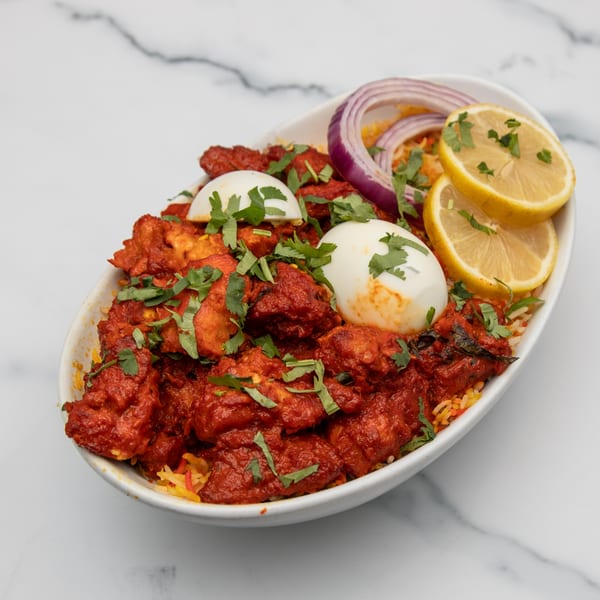 Mintt Indian Cuisine's chicken biryani, garnished with red onions, lemon slices, and cilantro.