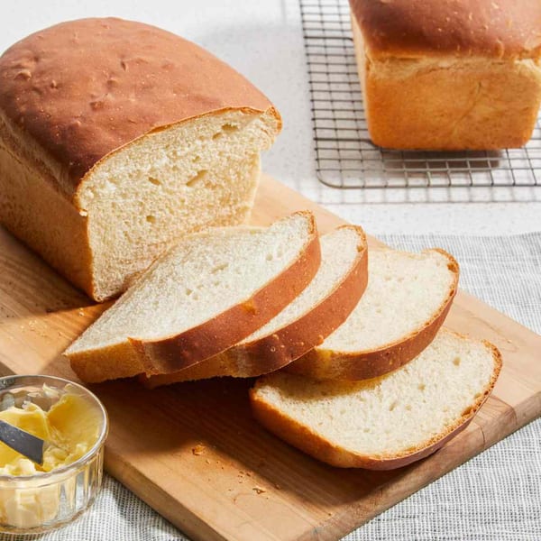 Freshly baked loaf of white bread, partially sliced, with a small dish of butter and knife.