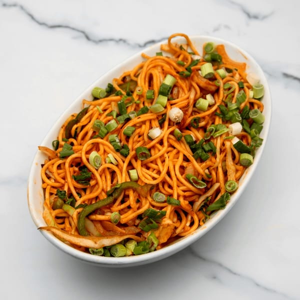 A white oval bowl filled with orange noodles, green onions, and vegetables on a marble surface.