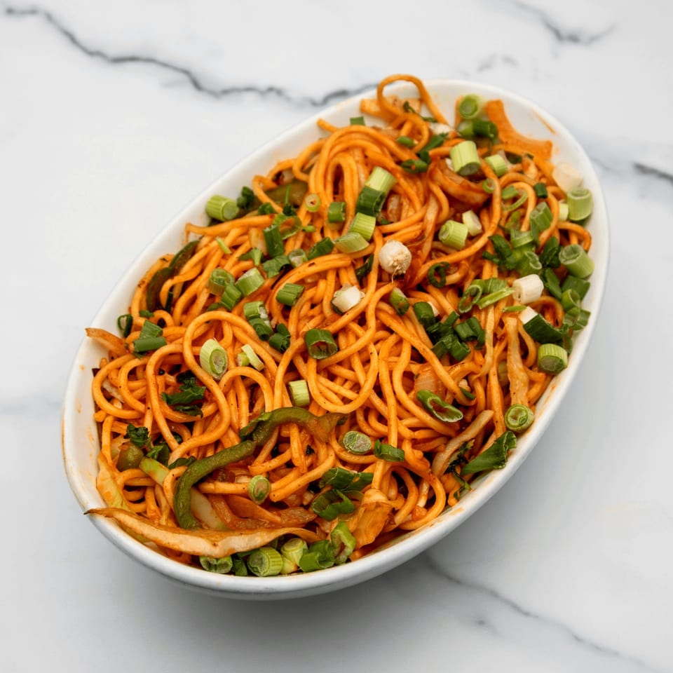 A white oval bowl filled with orange noodles, green onions, and vegetables on a marble surface.