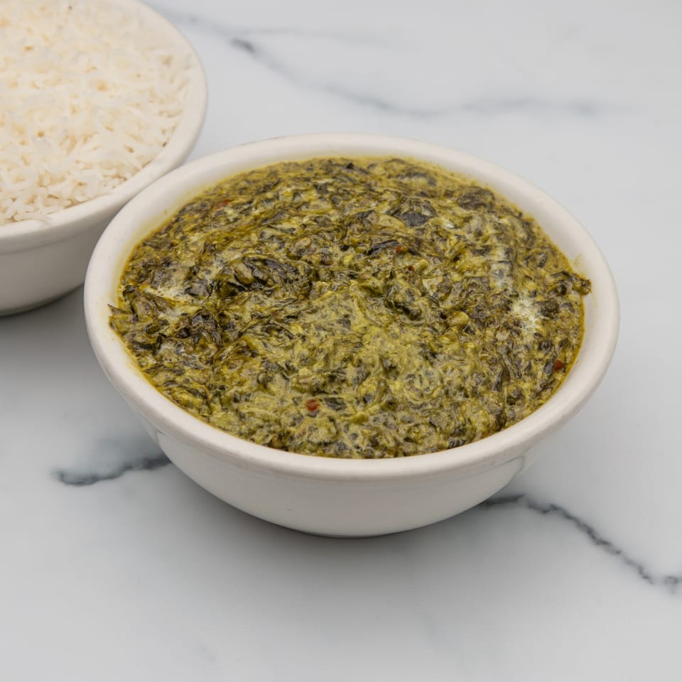 A bowl of vibrant green Indian palak paneer, with a bowl of white rice in the background.