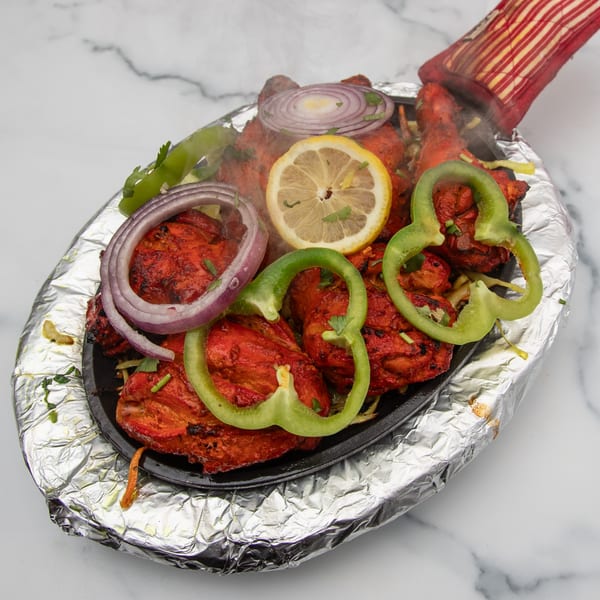 Sizzling Mintt Indian Cuisine tandoori chicken with onions, bell peppers, and lemon on a hot platter.