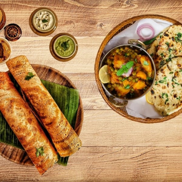 Indian food spread with dosas, curries, naan, and chutneys on a wooden table.