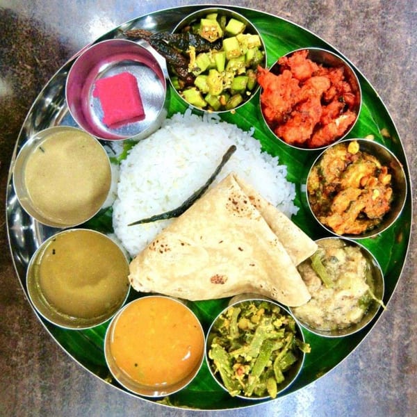 A traditional Indian thali meal with rice, flatbread, curries, and a pink dessert on a banana leaf.