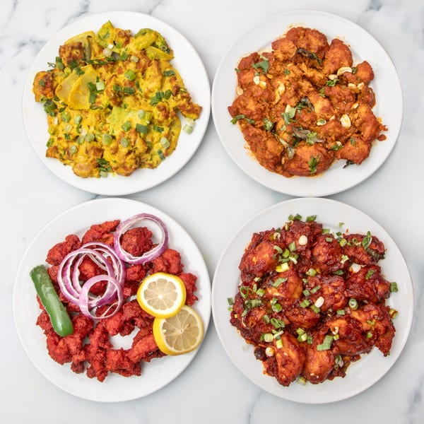 Four plates of Indian cuisine, including yellow scrambled eggs, red chicken dishes, and garnished with onions and lemons.