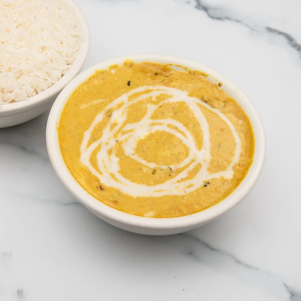 A bowl of creamy orange Indian curry with a white swirl, next to a bowl of white rice.