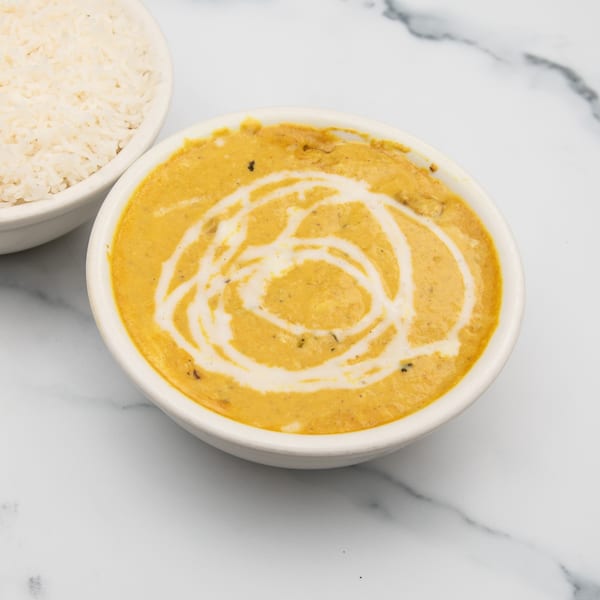 A bowl of creamy orange Indian curry with a white swirl, next to a bowl of white rice.
